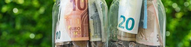 2 glass jar bottles with full of coins and euro banknotes with green bokeh in the background as investment or saving concept.