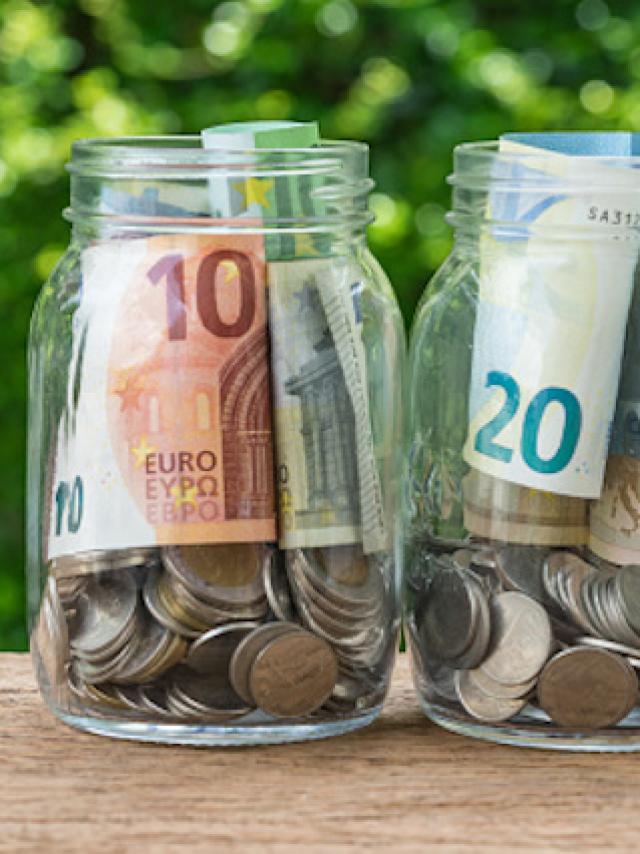 2 glass jar bottles with full of coins and euro banknotes with green bokeh in the background as investment or saving concept.